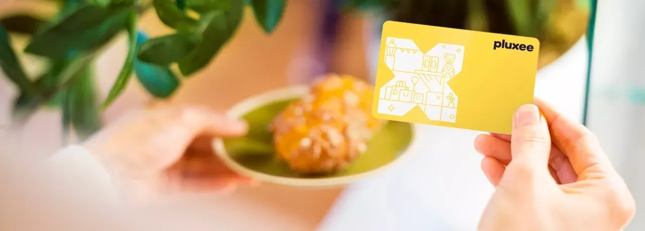 Eine Hand mit der Pluxee Benefits Card und ein Stück Kuchen