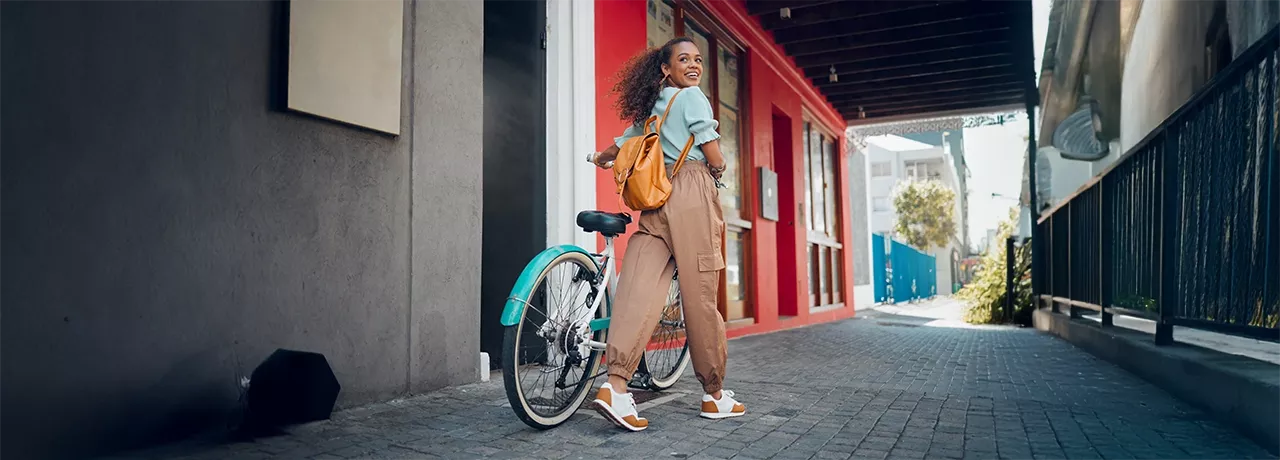 Junge Frau mit schwarzen lockigen Haaren fährt lächelnd auf einem türkisfarbenen Hollandrad – Symbolbild für modernes Bikeleasing und nachhaltige Mobilität. 