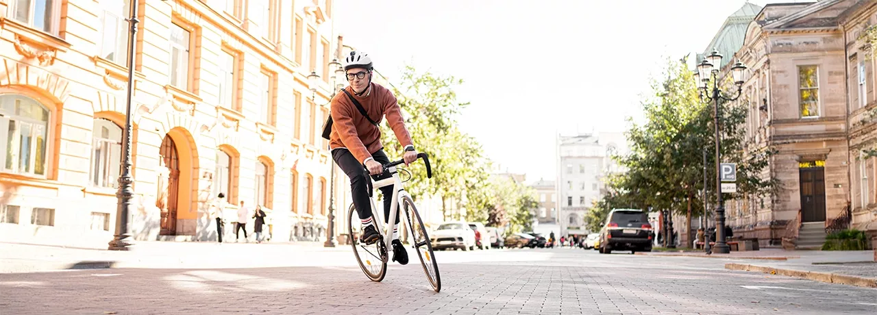 Mann mit Fahrradhelm fährt auf einem sportlichen Fahrrad durch die Stadt – auf dem Heimweg von der Arbeit, stellvertretend für umweltfreundliche Pendlerlösungen durch Bikeleasing. 