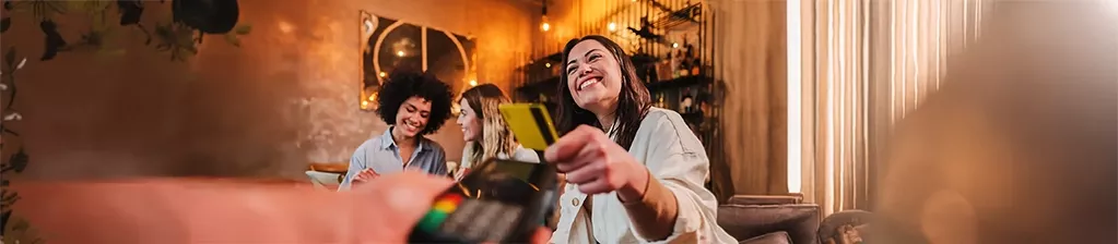 Drei Frauen in einem Restaurant genießen gemeinsam eine entspannte Zeit, eine davon bezahlt mit einer Karte – die Szene steht für Genuss, Gemeinschaft und die Benefits-Lösungen von Pluxee. 