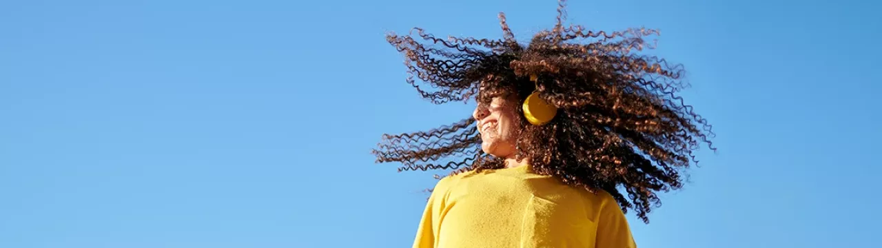Freudig tanzende Frau mit gelben Sweatshirt hört Musik über Ihre gelben Kopfhörer