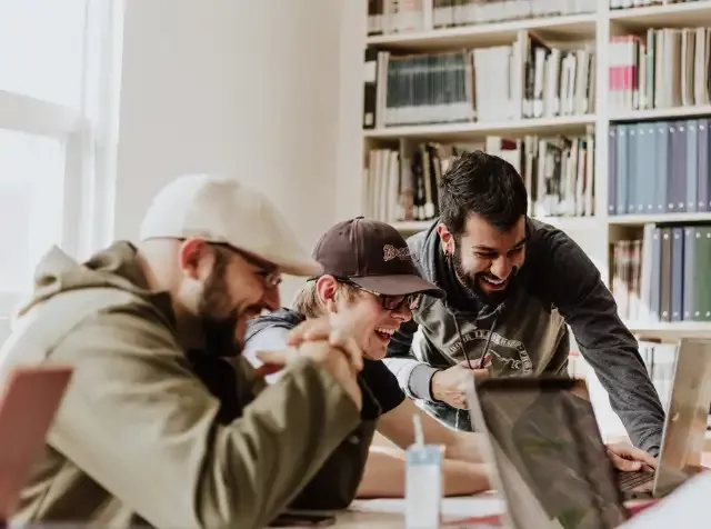 Drei Männer sitzen mit Laptops an einem Tisch und freuen sich über zahlreiche Sonderrabatte mit dem Pluxee Benefit Einkaufsrabatte.