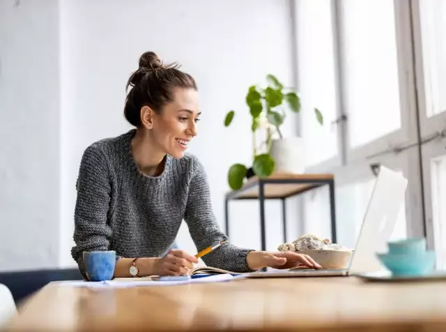 Eine Frau sitzt mit Laptop und Stift an einem Tisch und  freut sich über Mitarbeiterrabatte von ihrem Arbeitgeber, die von Pluxee optimiert wurden.