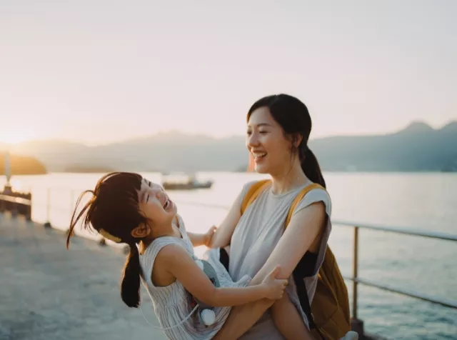 Glückliche Mutter und Tochter am Strand, lachen und genießen den Urlaub dank des Urlaubszuschusses von Pluxee.