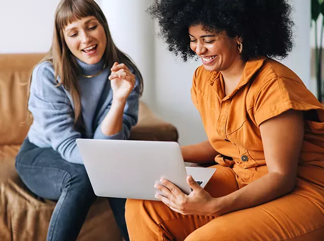 Zwei Frauen lachen vor einem Laptop