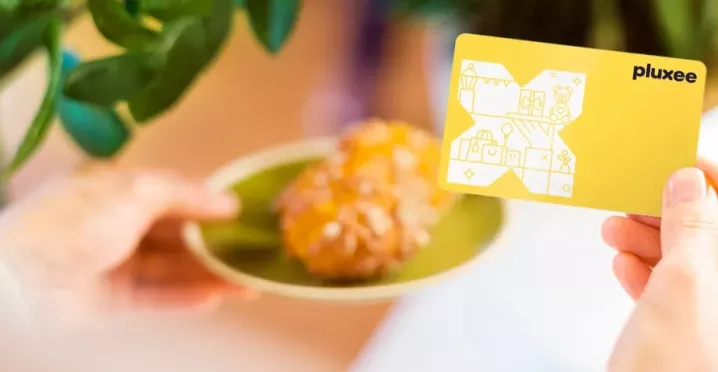 Eine Hand mit der Pluxee Benefits Card und ein Stück Kuchen