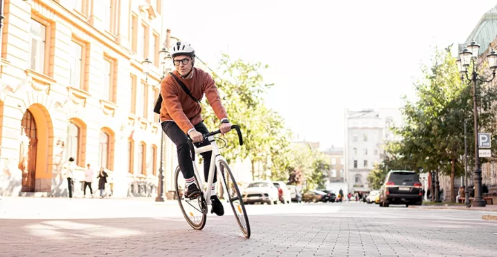 Mann mit Fahrradhelm fährt auf einem sportlichen Fahrrad durch die Stadt – auf dem Heimweg von der Arbeit, stellvertretend für umweltfreundliche Pendlerlösungen durch Bikeleasing.