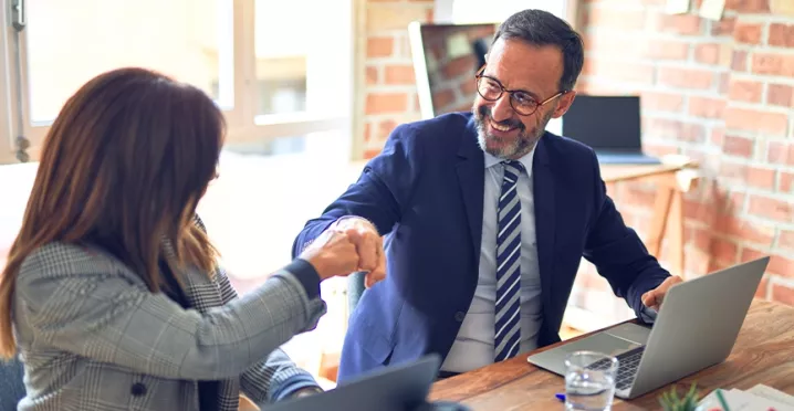Zwei Kolleg:innen feiern ihre erfolgreiche Zusammenarbeit mit einem Fistbump.