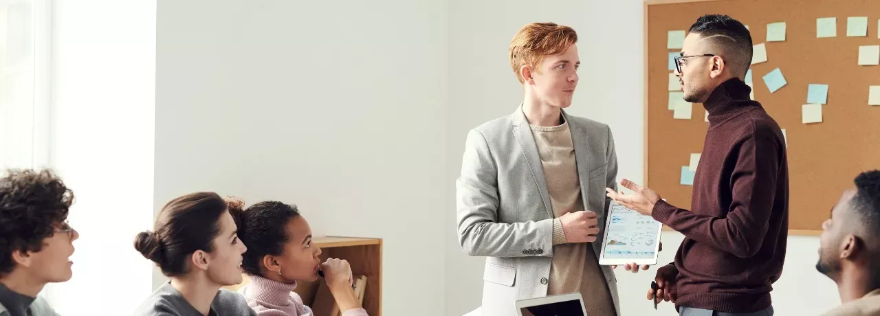 Zwei Menschen unterhalten sich vor einer Seminargruppe. 