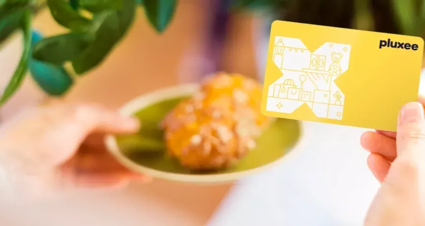 Eine Hand mit der Pluxee Benefits Card und ein Stück Kuchen