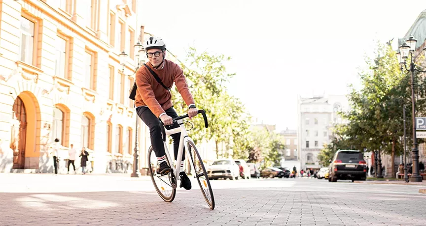 Mann mit Fahrradhelm fährt auf einem sportlichen Fahrrad durch die Stadt – auf dem Heimweg von der Arbeit, stellvertretend für umweltfreundliche Pendlerlösungen durch Bikeleasing.