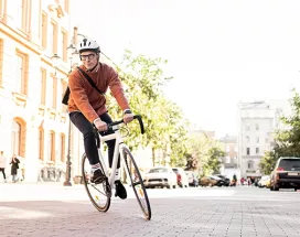 Mann mit Fahrradhelm fährt auf einem sportlichen Fahrrad durch die Stadt – auf dem Heimweg von der Arbeit, stellvertretend für umweltfreundliche Pendlerlösungen durch Bikeleasing.