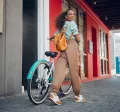 Junge Frau mit schwarzen lockigen Haaren fährt lächelnd auf einem türkisfarbenen Hollandrad – Symbolbild für modernes Bikeleasing und nachhaltige Mobilität.