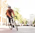 Mann mit Fahrradhelm fährt auf einem sportlichen Fahrrad durch die Stadt – auf dem Heimweg von der Arbeit, stellvertretend für umweltfreundliche Pendlerlösungen durch Bikeleasing.