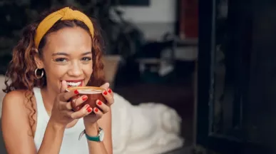 Frau lacht und hat es rote Kaffeetasse in der Hand. 