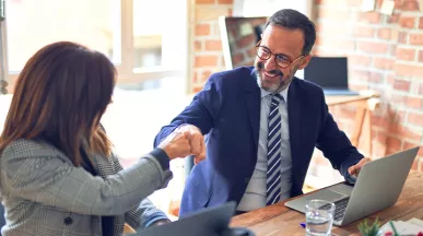 Zwei Kolleg:innen feiern ihre erfolgreiche Zusammenarbeit mit einem Fistbump.