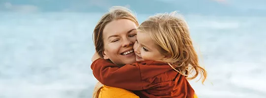 Mutter und Kind umarmen sich am Strand vor dem Meer