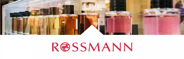Mehrere Parfüm-Flaschen stehen in einer Reihe auf einem Regal, darunter das Logo 'ROSSMANN' in roter Schrift.